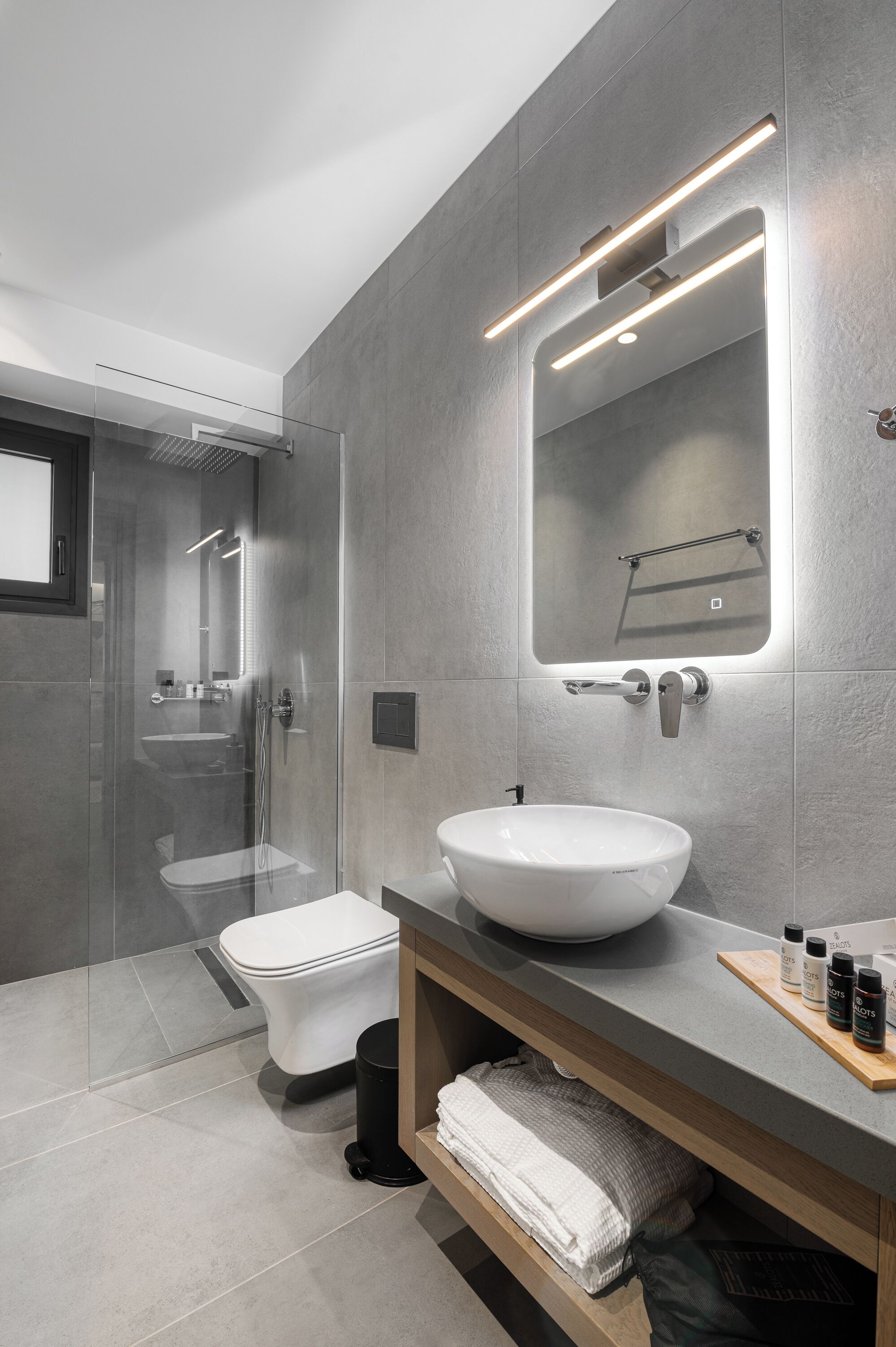 Een moderne badkamer met een douchecabine van glas, een wit wastafelmeubel en een spiegel met ingebouwde verlichting.