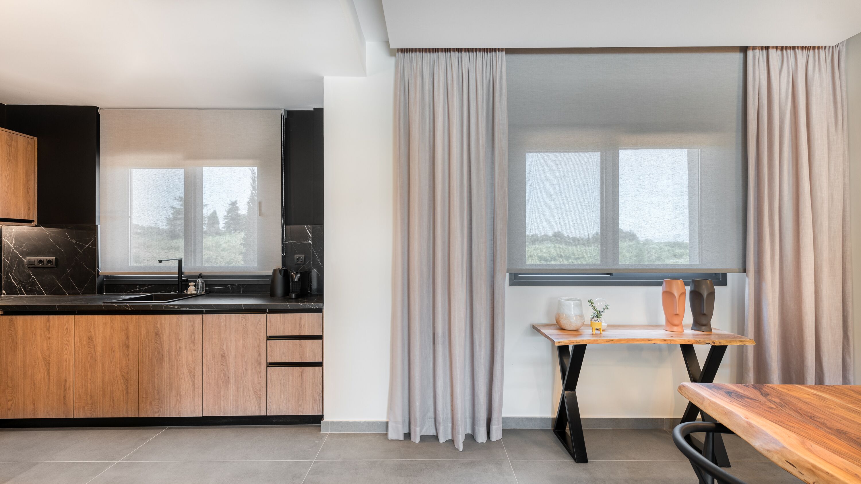 Una cuina moderna amb armaris de fusta, un taulell negre i una finestra amb cortines.