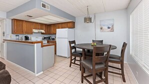 A compact kitchen with wooden cabinets, a central island, and a dining area with four chairs. - 2 Bed 2 Bath 1st Fl Condo By Beach w Washer/Dryer (South Padre Island)