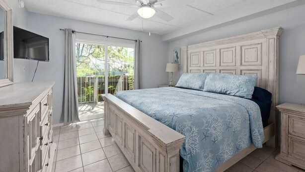 A bedroom with a large bed, a ceiling fan, a TV mounted on the wall, and a sliding glass door leading to an outdoor area. - 2 Bed 2 Bath 1st Fl Condo By Beach w Washer/Dryer (South Padre Island)