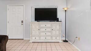 A room with a white door, a white cabinet with drawers, a flat-screen TV mounted above the cabinet, and a floor lamp to the right. - 2 Bed 2 Bath 1st Fl Condo By Beach w Washer/Dryer (South Padre Island)