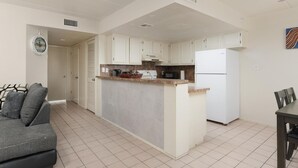 A compact kitchen with white cabinets, a central island, and a dining area with a table and chairs. - Lovely 2 Bed 2 Bath 2nd Floor Condo By Beach (South Padre Island)