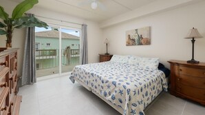 A bedroom with a bed, a nightstand, a lamp, a painting, and a view of a balcony. - Lovely 2 Bed 2 Bath 2nd Floor Condo By Beach (South Padre Island)