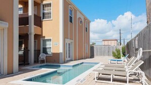 A swimming pool with lounge chairs and a shower sign, surrounded by a building with balconies and a wooden fence. - Beautiful 3 Bed 2 Bath 1st Floor Condo Near Beach (South Padre Island)