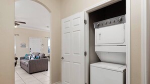 A laundry room with a stacked washer and dryer, a closed door, and a living area with a sofa and pillows. - Beautiful 3 Bed 2 Bath 1st Floor Condo Near Beach (South Padre Island)