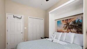 A bedroom with a bed, two white doors, and a painting of palm trees. - Beautiful 3 Bed 2 Bath 1st Floor Condo Near Beach (South Padre Island)