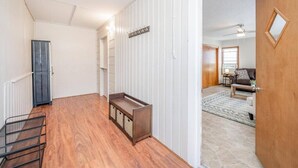 A hallway with a wooden bench, a coat rack, and a door leading to a living area with a couch and a rug.