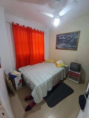 Ein Schlafzimmer mit einem Bett, einem Fernseher auf einem Schrank, einem Bild an der Wand und einem roten Vorhang.