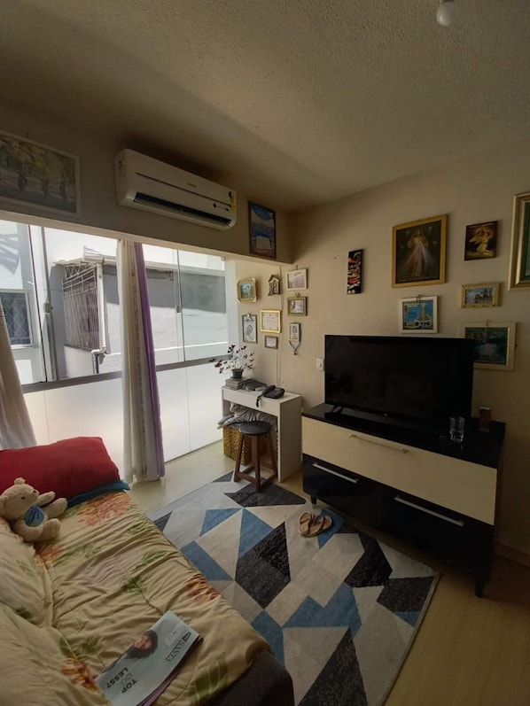 Ein kleines Hotelzimmer mit Bett, Schreibtisch mit Stuhl, Fernseher und einem Fenster mit Vorhängen.