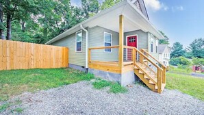Une maison de plain-pied avec une porte rouge, un escalier en bois et une clôture en bois.