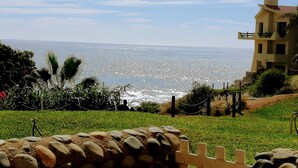 Blick auf die Küste mit einer Steinmauer, einer Rasenfläche und einem Gebäude mit Balkon zum Meer.