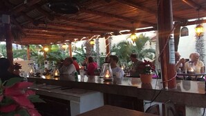 Ein Restaurant im Freien mit Holzboden, Tischen und Stühlen, umgeben von Palmen und Topfpflanzen.
