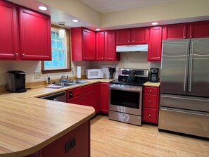 Una cocina con gabinetes rojos, electrodomésticos de acero inoxidable, un microondas y una cafetera.