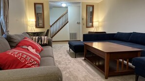 A living room with a grey sofa, a blue sectional, and a wooden coffee table. There is a staircase leading to another room. - Peaceful Farmhouse & Rural Views (Sabina)