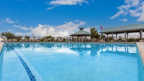 Una piscina azul cristalina con sillas de descanso y un pabellón.