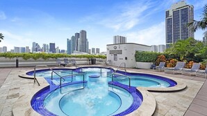 Ein Pool auf dem Dach mit mehreren Whirlpools, umgeben von Liegestühlen und einer Skyline im Hintergrund.