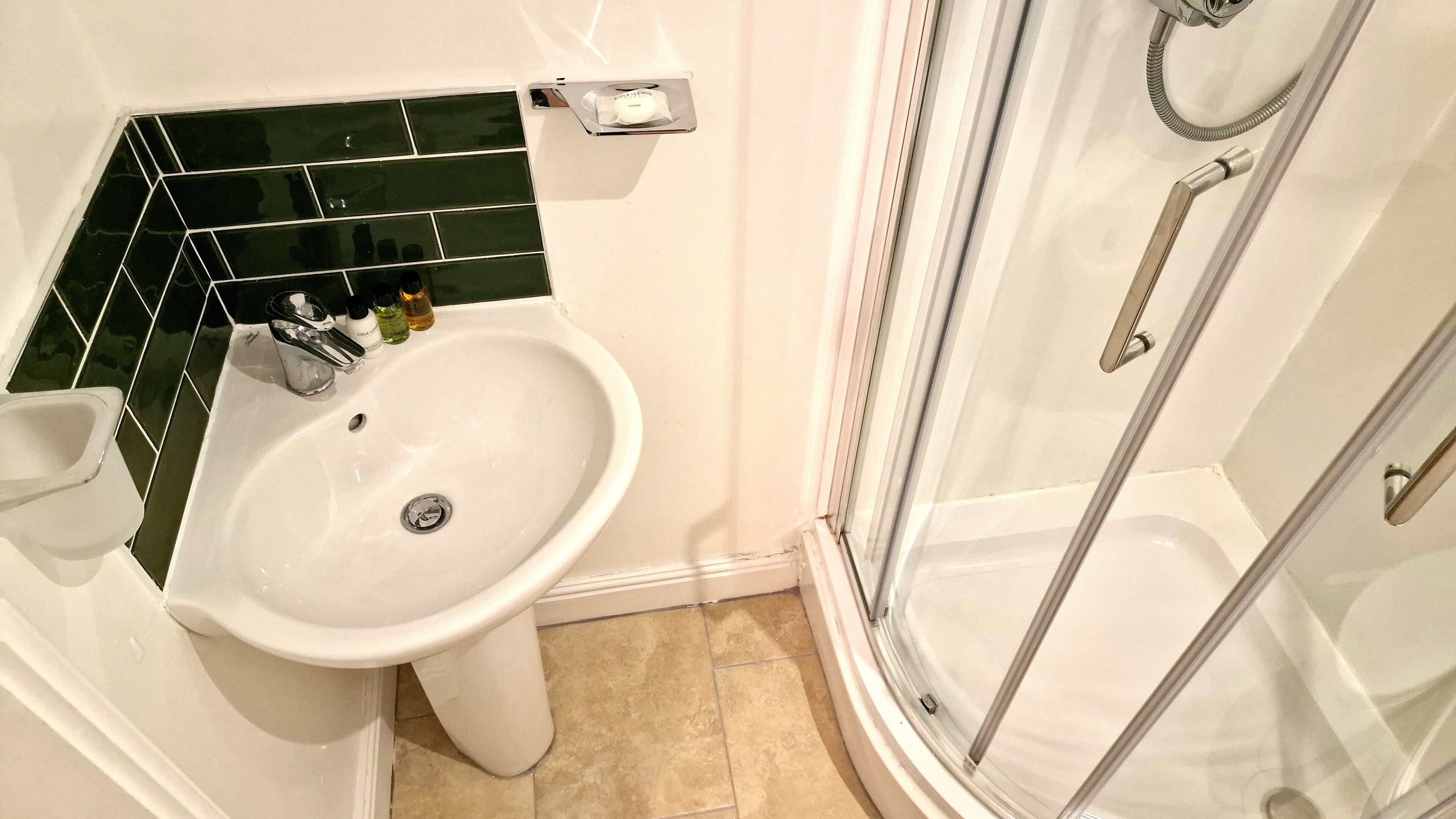 Une salle de bain avec un lavabo blanc, une douche en verre et un mur recouvert de carreaux verts derrière le lavabo.