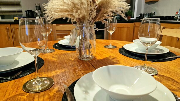 A dining table set with white plates, silver cutlery, and clear wine glasses. A vase with dried pampas grass is placed in the center. - Stunning Luxury 2 Bed City Centre Apartment (Derby)