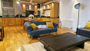 Un soggiorno moderno con un divano blu, un tavolino in legno e un'area pranzo con pensili in legno e uno schienale piastrellato nero.