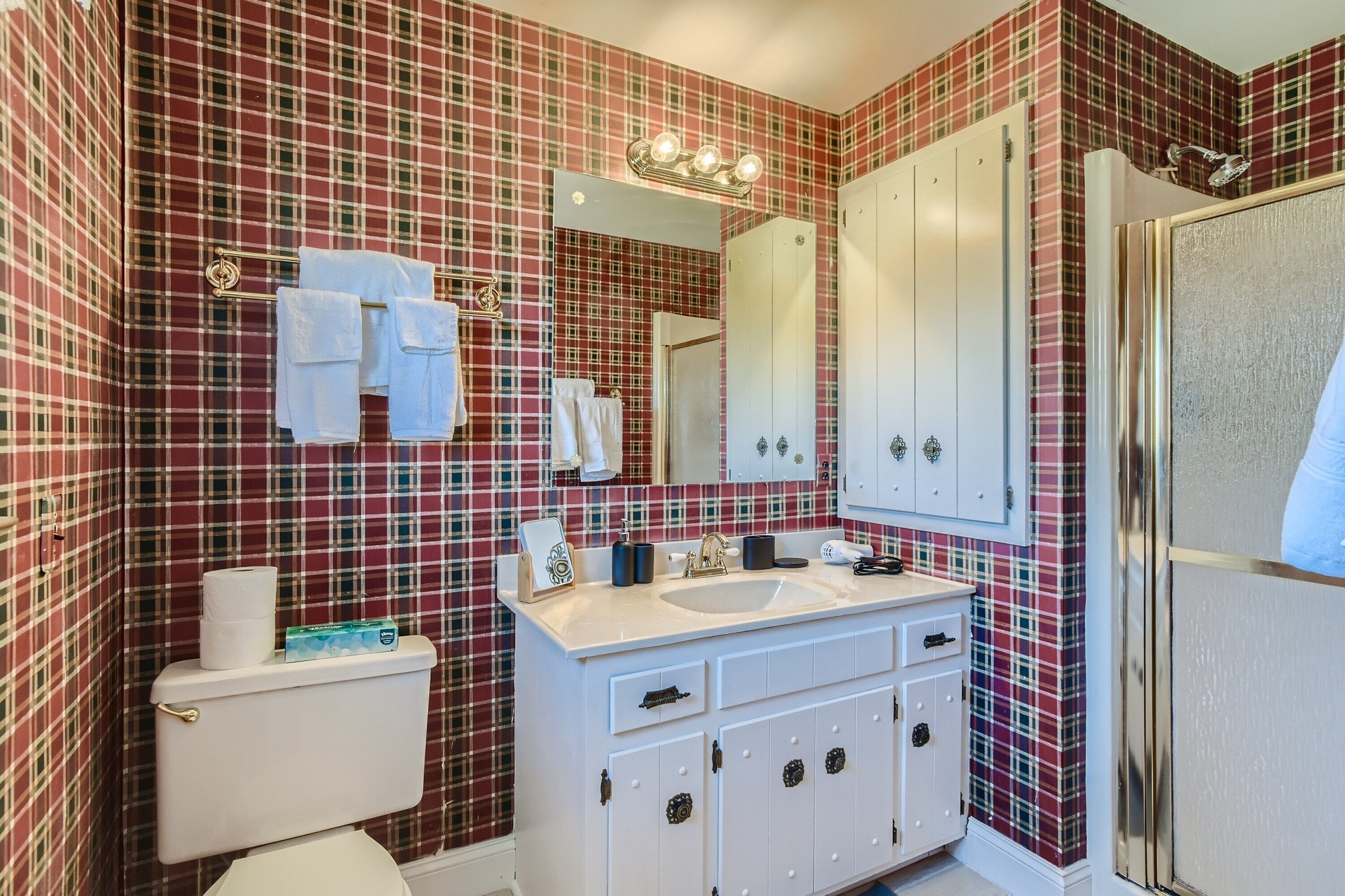 Un baño con papel tapiz estampado en cuadros, un lavabo blanco y un espejo encima.