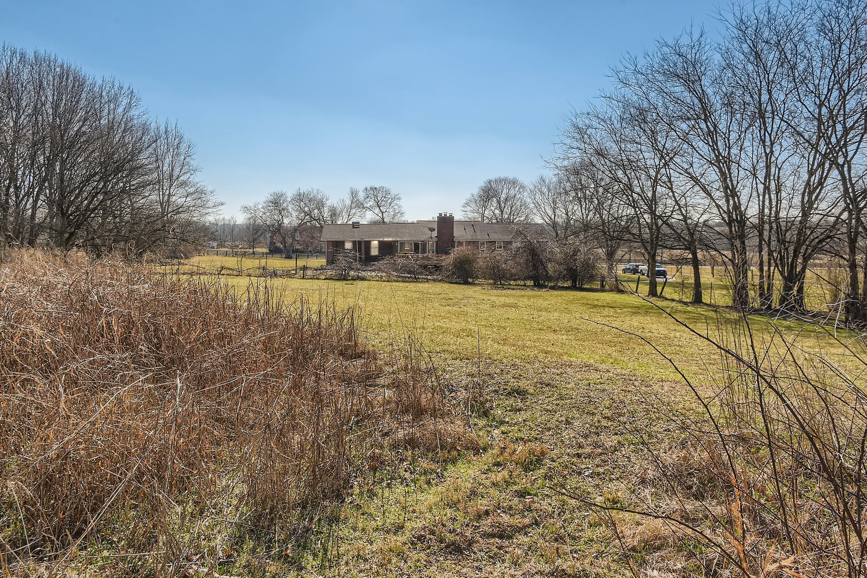 Ein großes, zweistöckiges Haus mit einem markanten Schornstein, umgeben von einer Wiese und kahlen Bäumen.