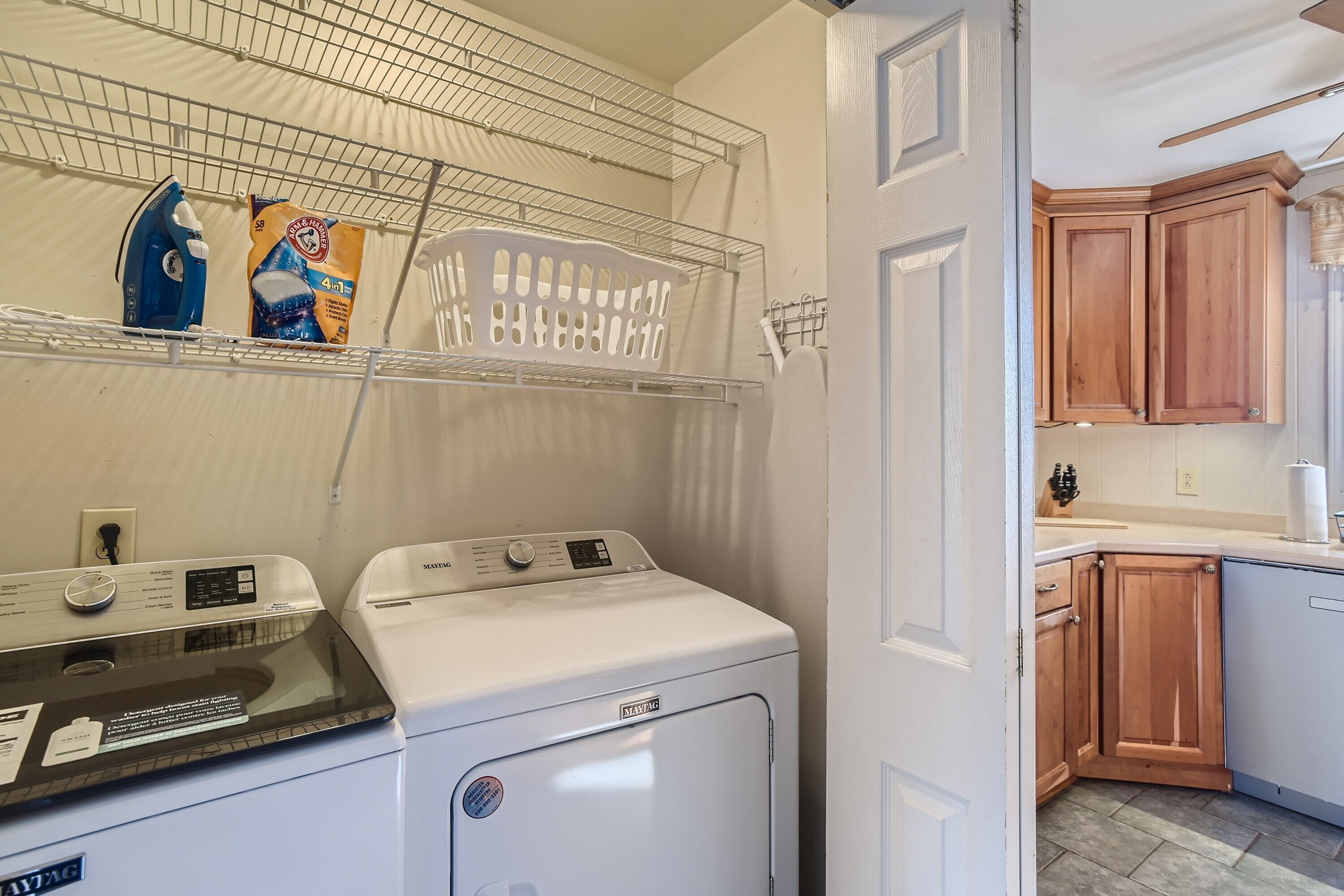 A laundry area with two washing machines, a drying rack, and a shelf with laundry supplies.
