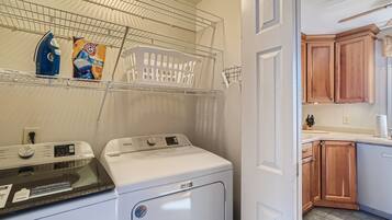 A laundry area with two washing machines, a drying rack, and a shelf with laundry supplies.
