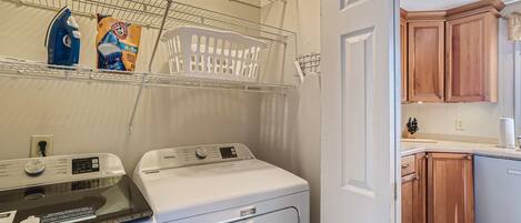 A laundry area with two washing machines, a drying rack, and a shelf with laundry supplies.