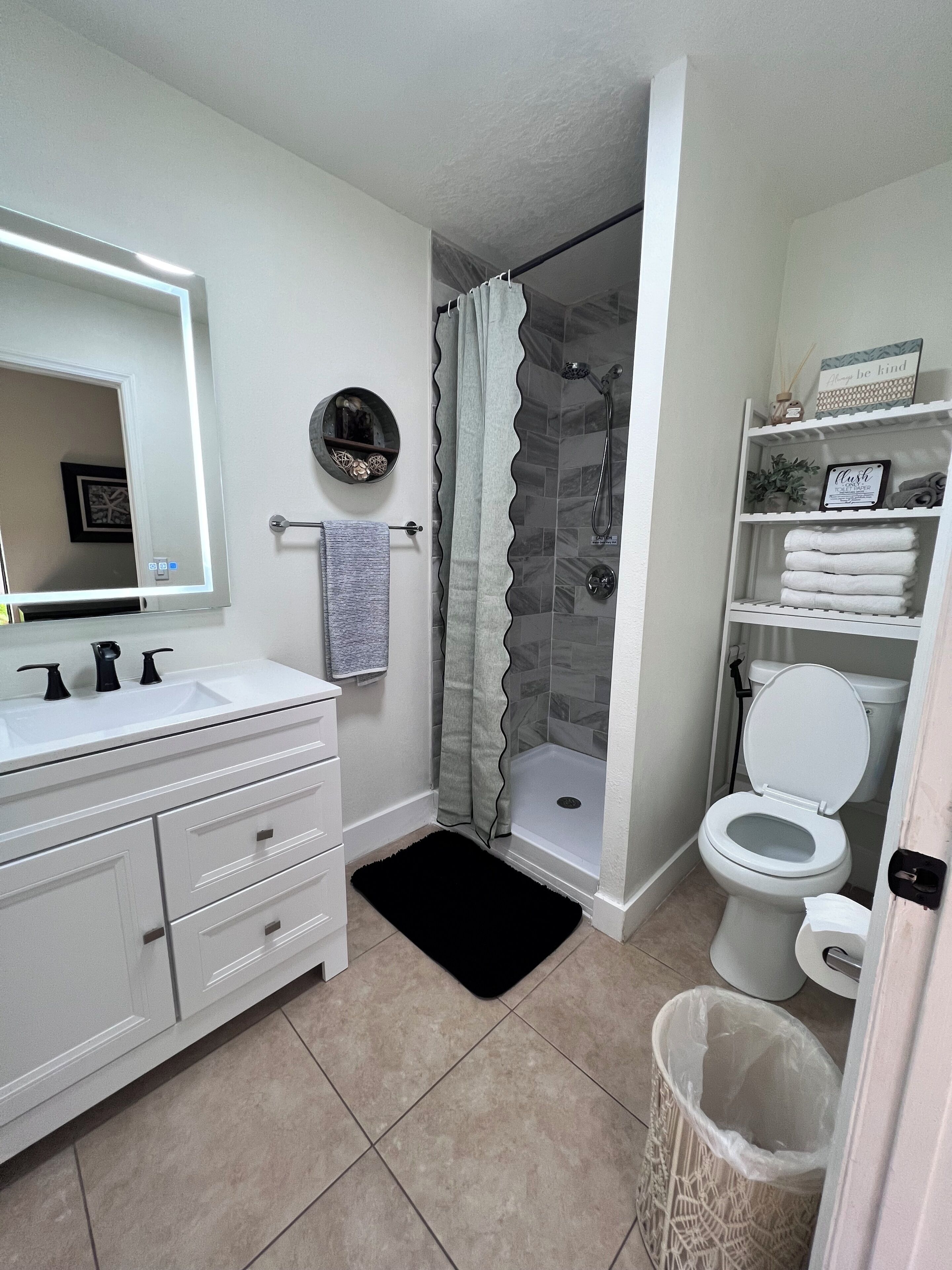 Une salle de bain avec un meuble-lavabo blanc, une douche avec une porte en verre, des toilettes et une poubelle.