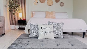 Un dormitorio con cama, almohadas, mesita de noche, lámpara, planta en maceta y decoración mural.