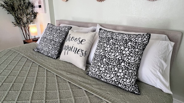 Una cama con un edredón verde, cuatro almohadas con diseños florales y una pared decorada con adornos circulares.