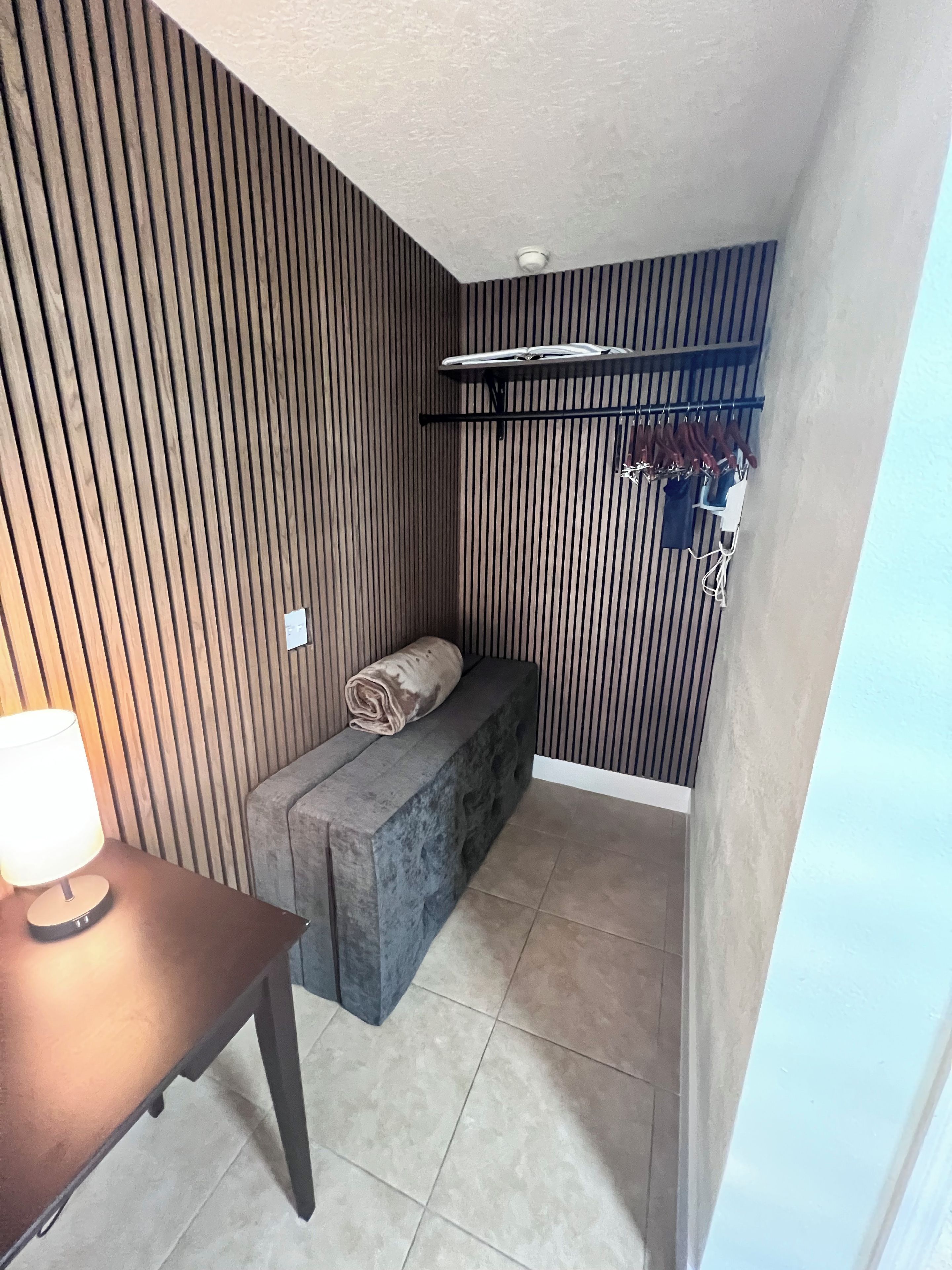 Une pièce d’angle avec un banc, un portant à vêtements suspendu et une lampe sur une table.