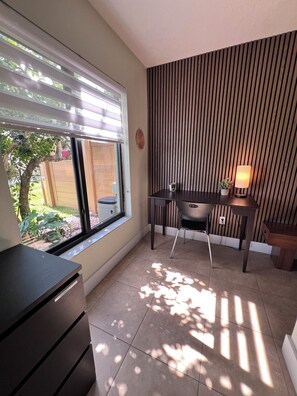 Una habitación con escritorio, silla y ventana con persianas.