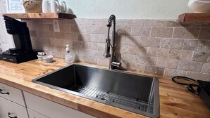 Una cocina con un lavamanos de acero inoxidable, encimera de madera, armarios blancos, una cafetera y un letrero en la pared que dice 'café latte'.