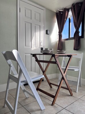 A compact room with a white door, a window with curtains, a small table, and two white chairs.