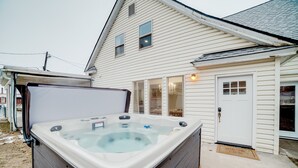 A hot tub in front of a white house with a garage and a door.