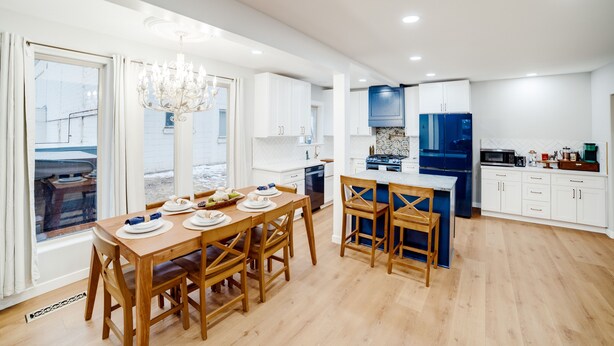 A modern kitchen with white cabinets, a blue refrigerator, and a wooden dining table set for four.