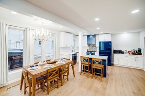 Una cocina moderna con armarios blancos, un refrigerador azul y una mesa de comedor de madera dispuesta para cuatro personas.