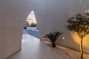 Un couloir avec un sol carrelé, une petite plante et un luminaire fixé au mur.
