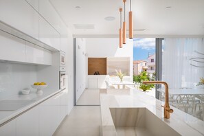 A modern kitchen with white cabinetry, a marble countertop, and a copper faucet.