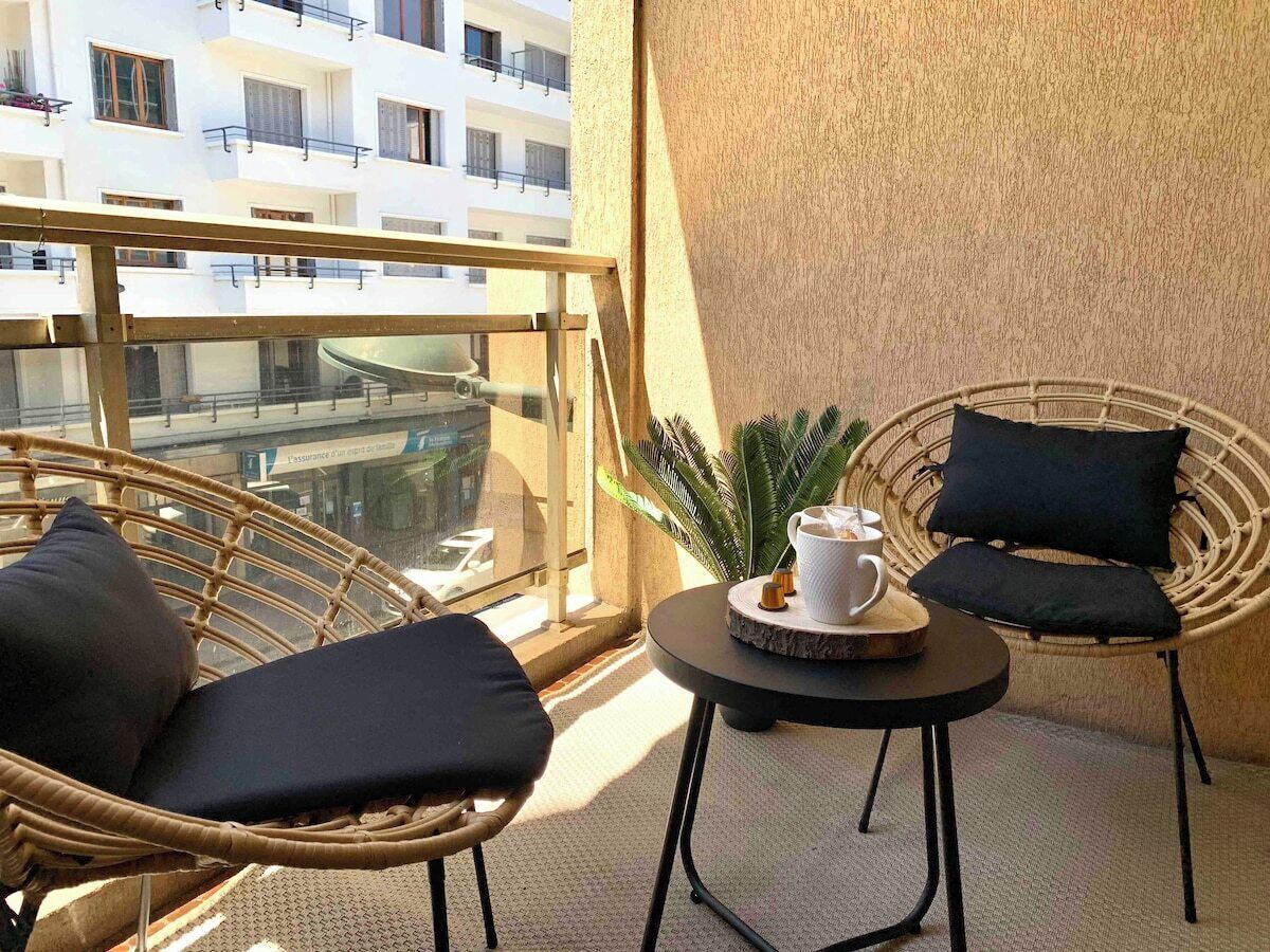 Un balcon avec des fauteuils en osier, une petite table ronde sur laquelle se trouve une tasse de café et une plante en pot.
