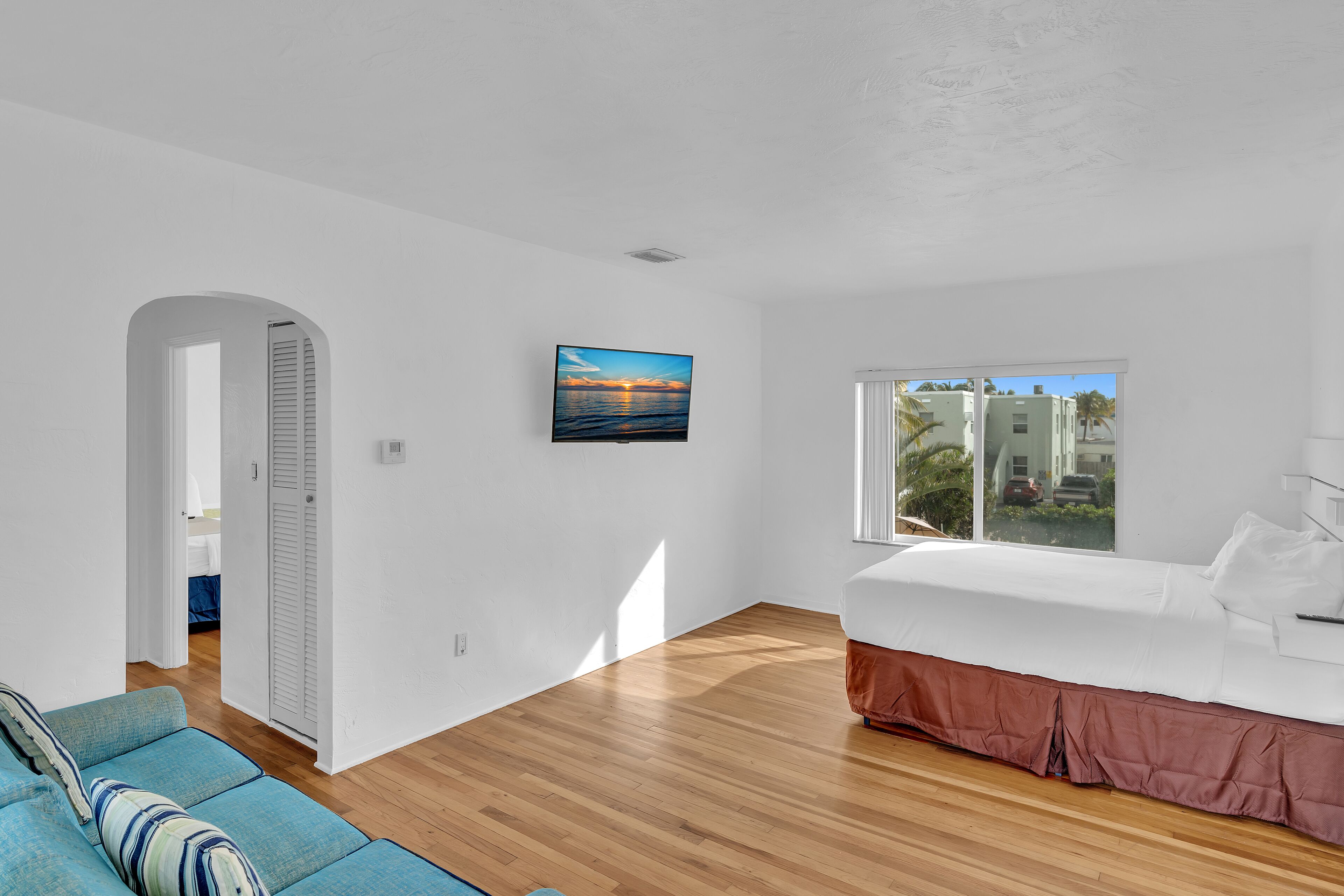 A modern bedroom with a large window, a bed, a blue sofa, and a painting on the wall.