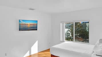 Un dormitorio con cama, ventana con vistas a edificios y un cuadro en la pared.