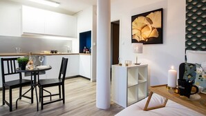 A modern hotel room with a dining area, a bedside table with a lamp, and a bed with a floral pillow. - Biloba du Lac (Annecy)