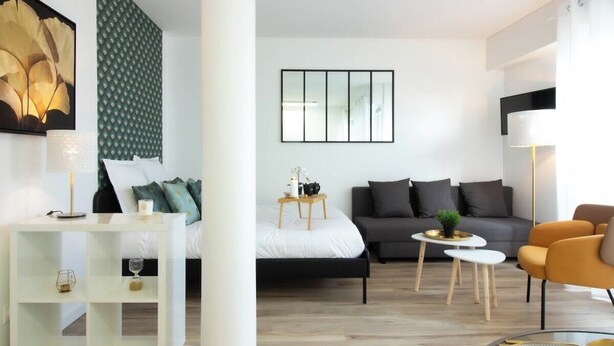 A modern hotel room with a bed, a sofa, a small table, and a chair. There is a wall art piece above the bed and a framed picture on the wall. - Biloba du Lac (Annecy)