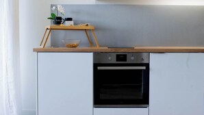 A kitchen with a built-in oven, a wooden countertop, and a small shelf with a coffee cup and a plant. - Biloba du Lac (Annecy)