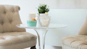 A round table with a clear glass top, a white mug, a small blue cup, and a clear glass vase with a plant. - Lafayette 2 vélos proche du lac (Annecy)