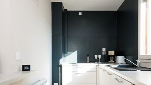 A modern kitchen with white cabinets, a black trash bin, and a radiator. - Lafayette 2 vélos proche du lac (Annecy)