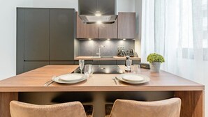 A modern kitchen with a large dining table, dark cabinets, and a built-in stove. - Loge Galeries Lafayette 1 min lac (Annecy)