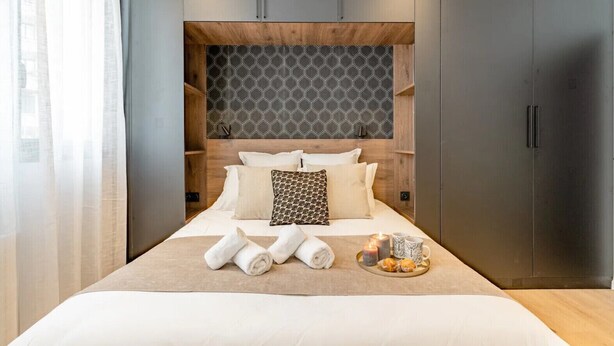 A modern bedroom with a large bed, wooden headboard, and a tray with towels and pastries. - Loge Galeries Lafayette 1 min lac (Annecy)